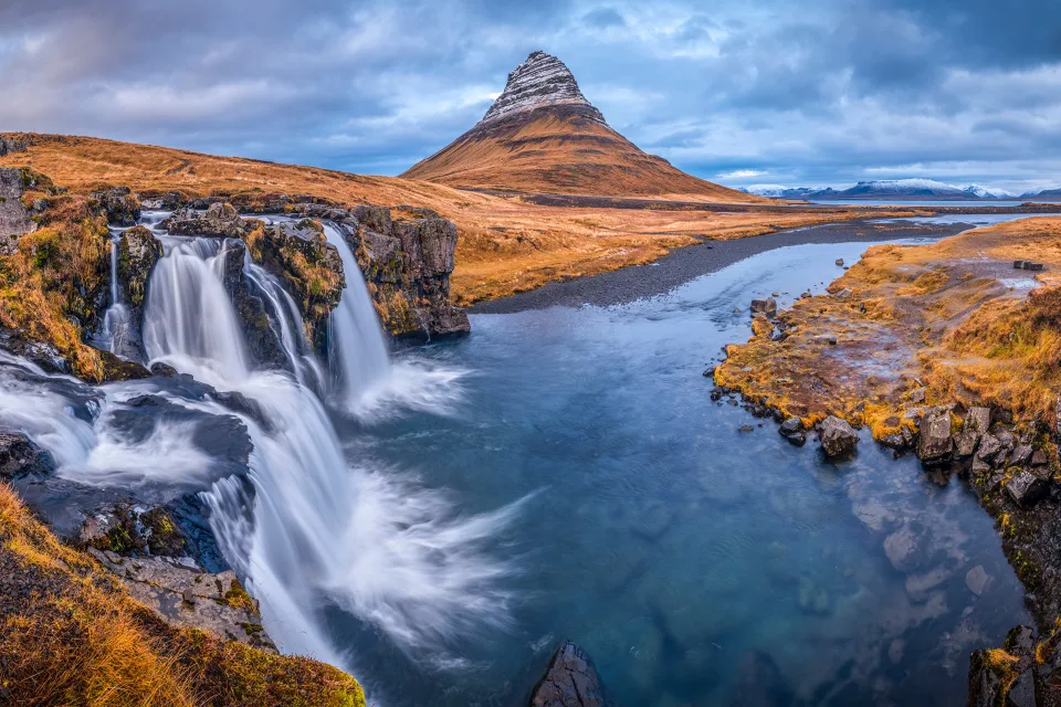 Blick auf Fluss, Wasserfall und Berg unter bewölktem Himmel