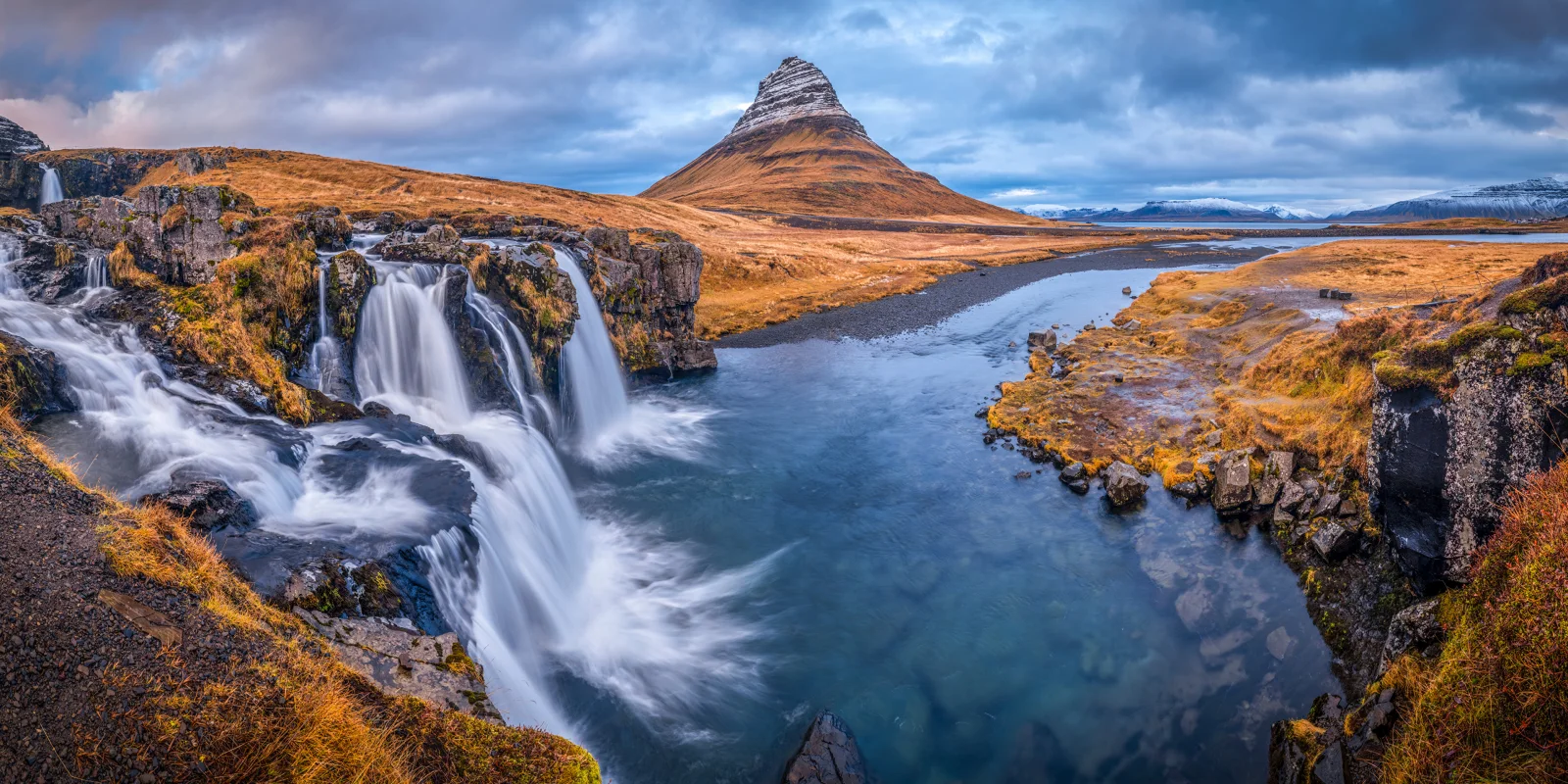 Blick auf Fluss, Wasserfall und Berg unter bewölktem Himmel