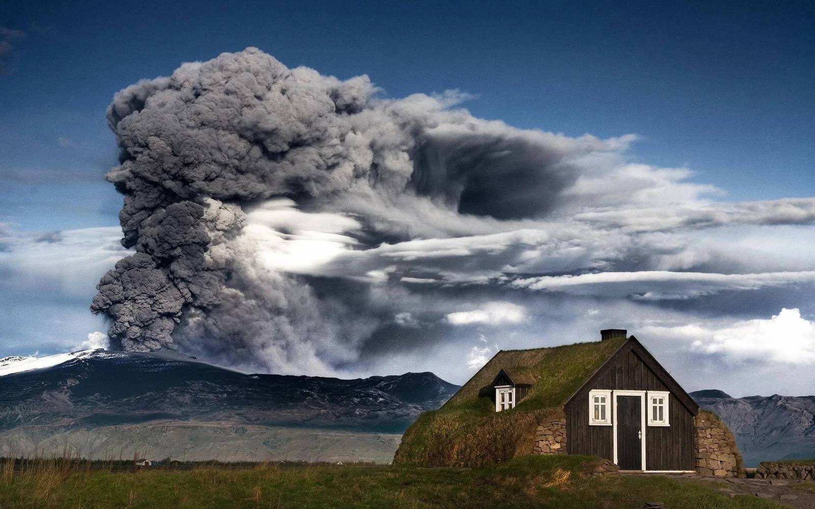 Haus in Island vor dem Hintergrund ausbrechenden Vulkan