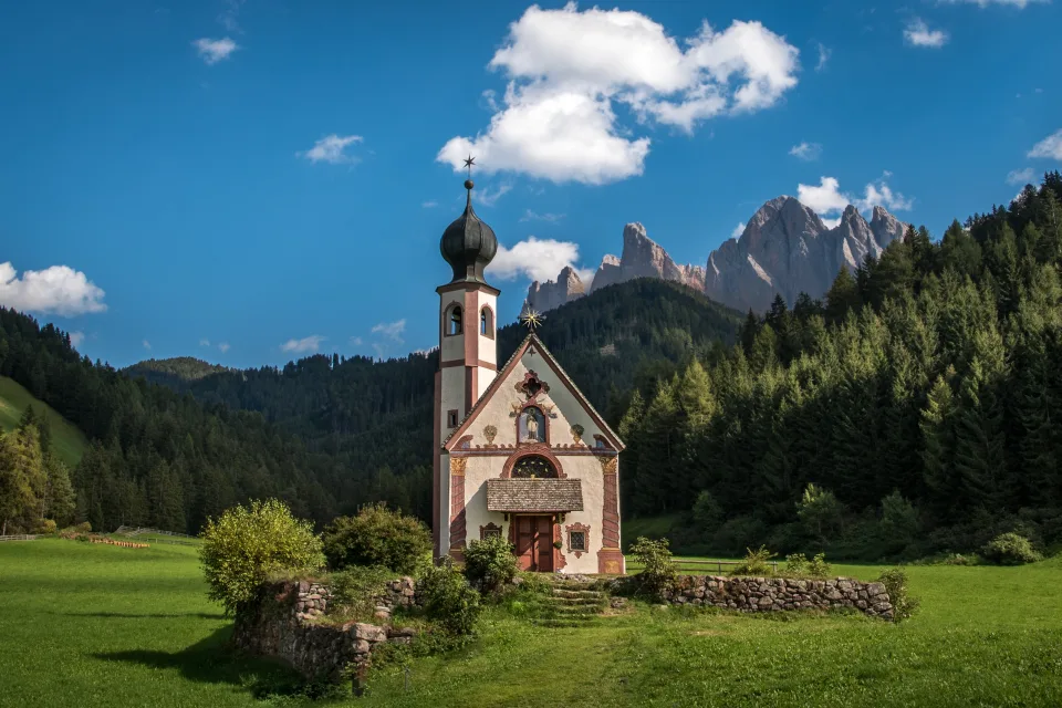 Alte Kirche vor einer Bergkulisse unter schönem hellblauem Himmel, Italien