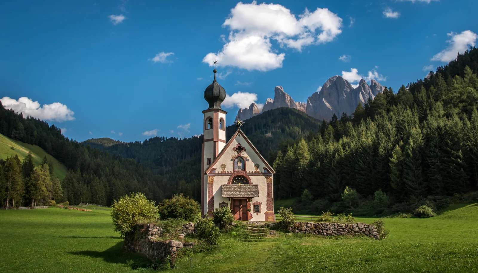 Alte Kirche vor einer Bergkulisse unter schönem hellblauem Himmel, Italien