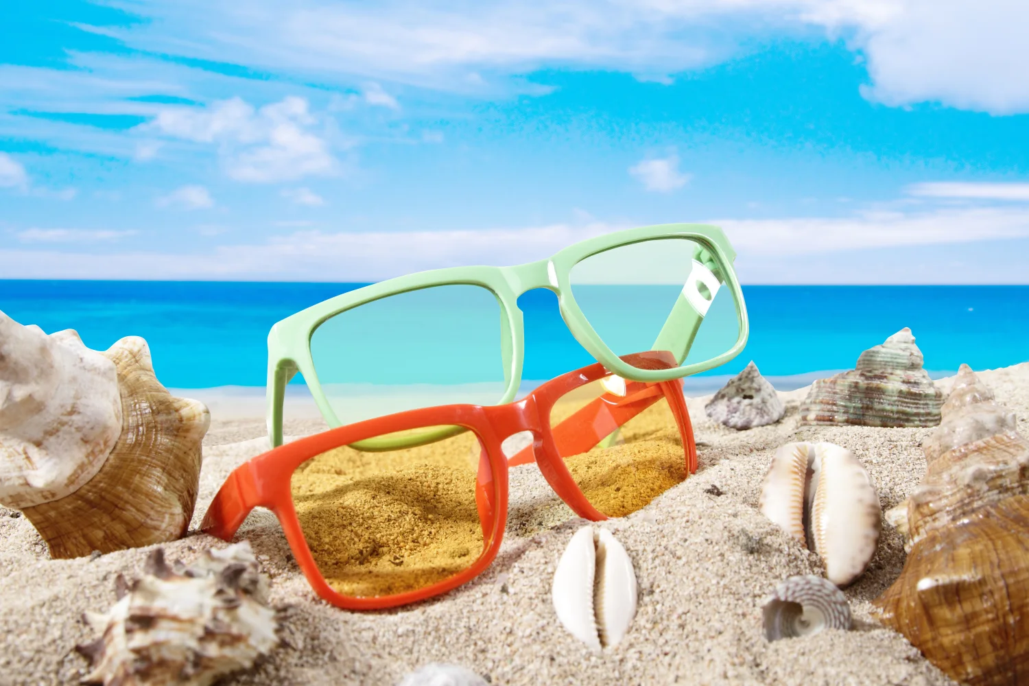 Brille im Sand mit Muscheln am Meer im Sommer