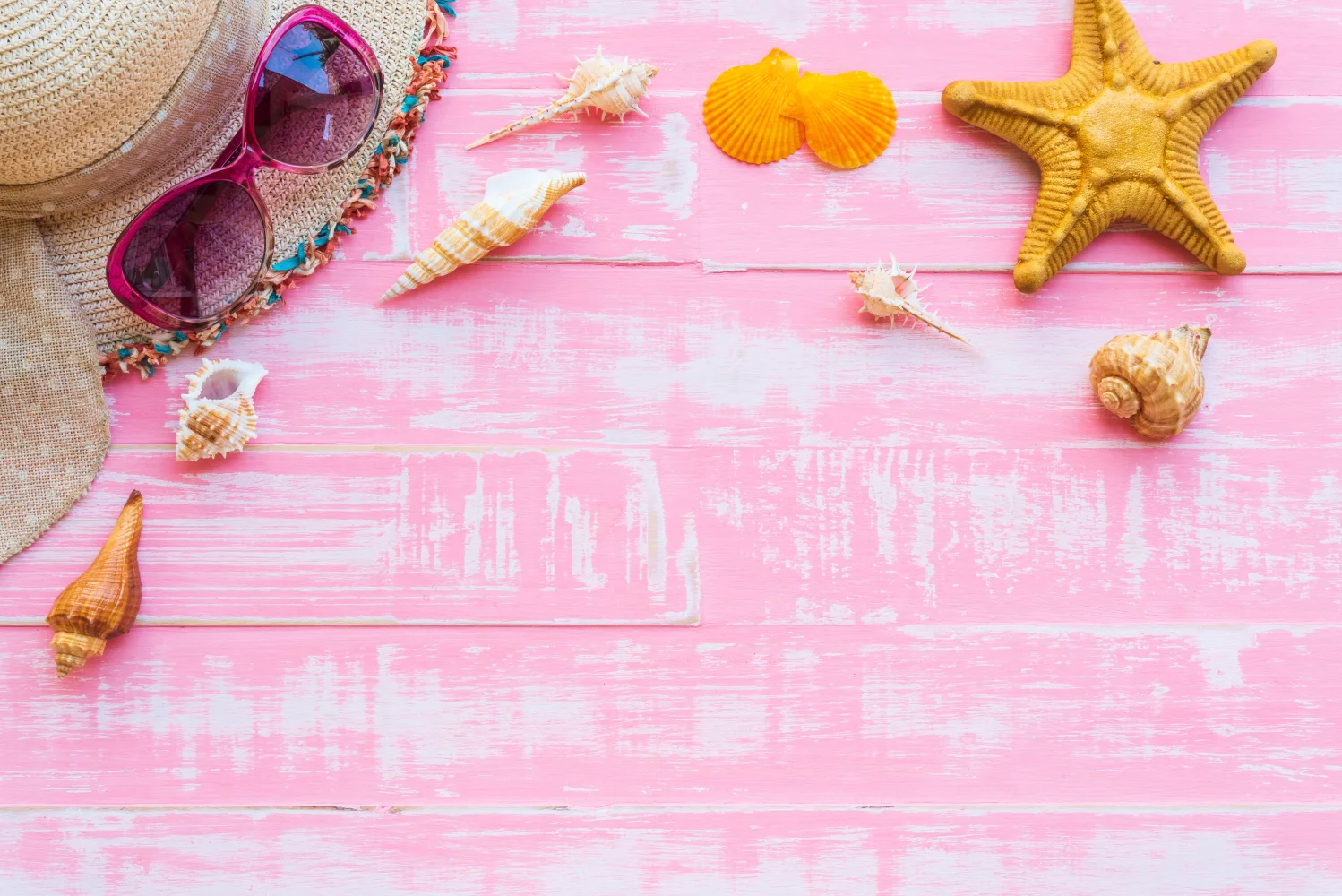 Muscheln, Brille und Hut vor rosa Hintergrund