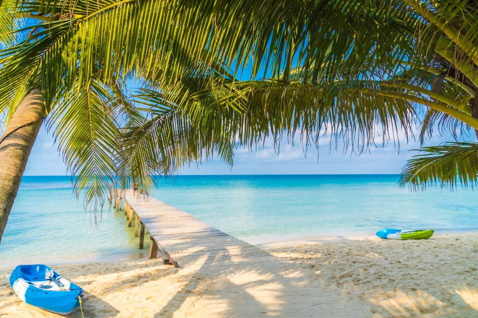 Weißer Sand am Strand mit Palmen bei Ozean mit hellblauer Wasser im Sommer