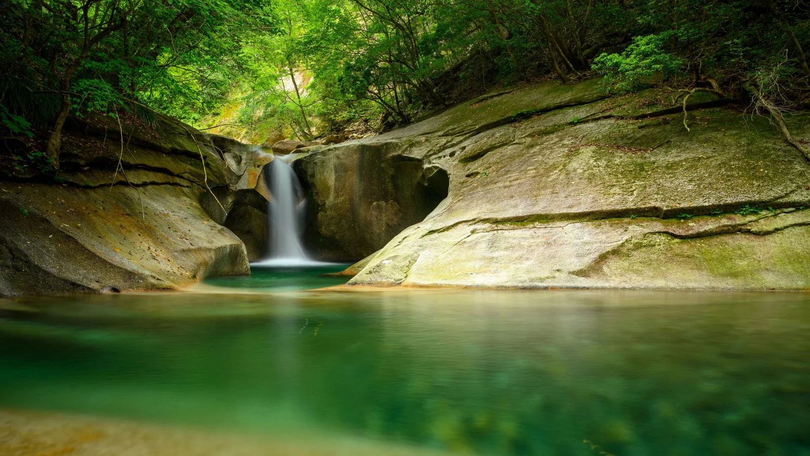 Wasserfall fließt entlang Felsen in See im Wald