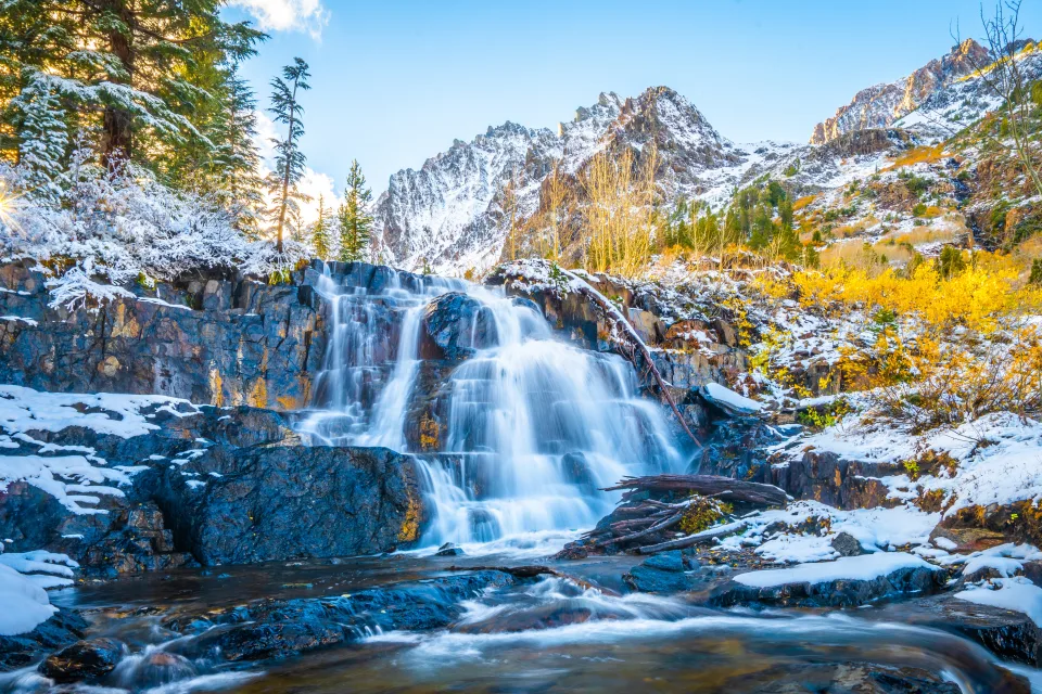 Wasserfall fließt entlang bedecktem Schnee Felsen in den Bergenn