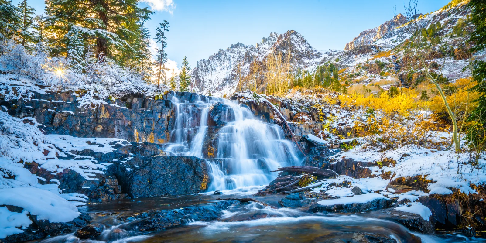 Wasserfall fließt entlang bedecktem Schnee Felsen in den Bergenn