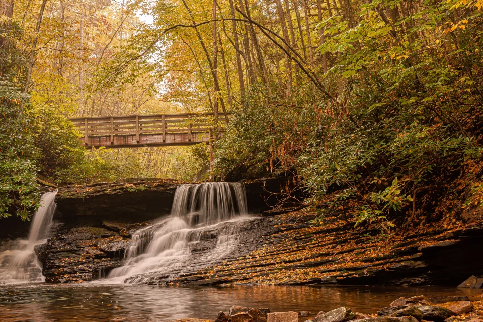 Wasserfall fließt über Steine unter Brücke im Herbst