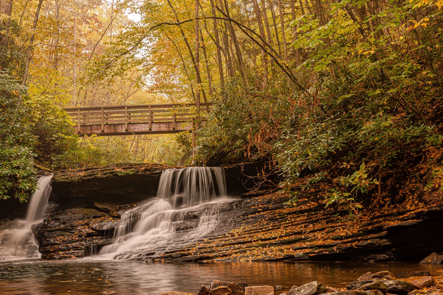 Wasserfall fließt über Steine unter Brücke im Herbst