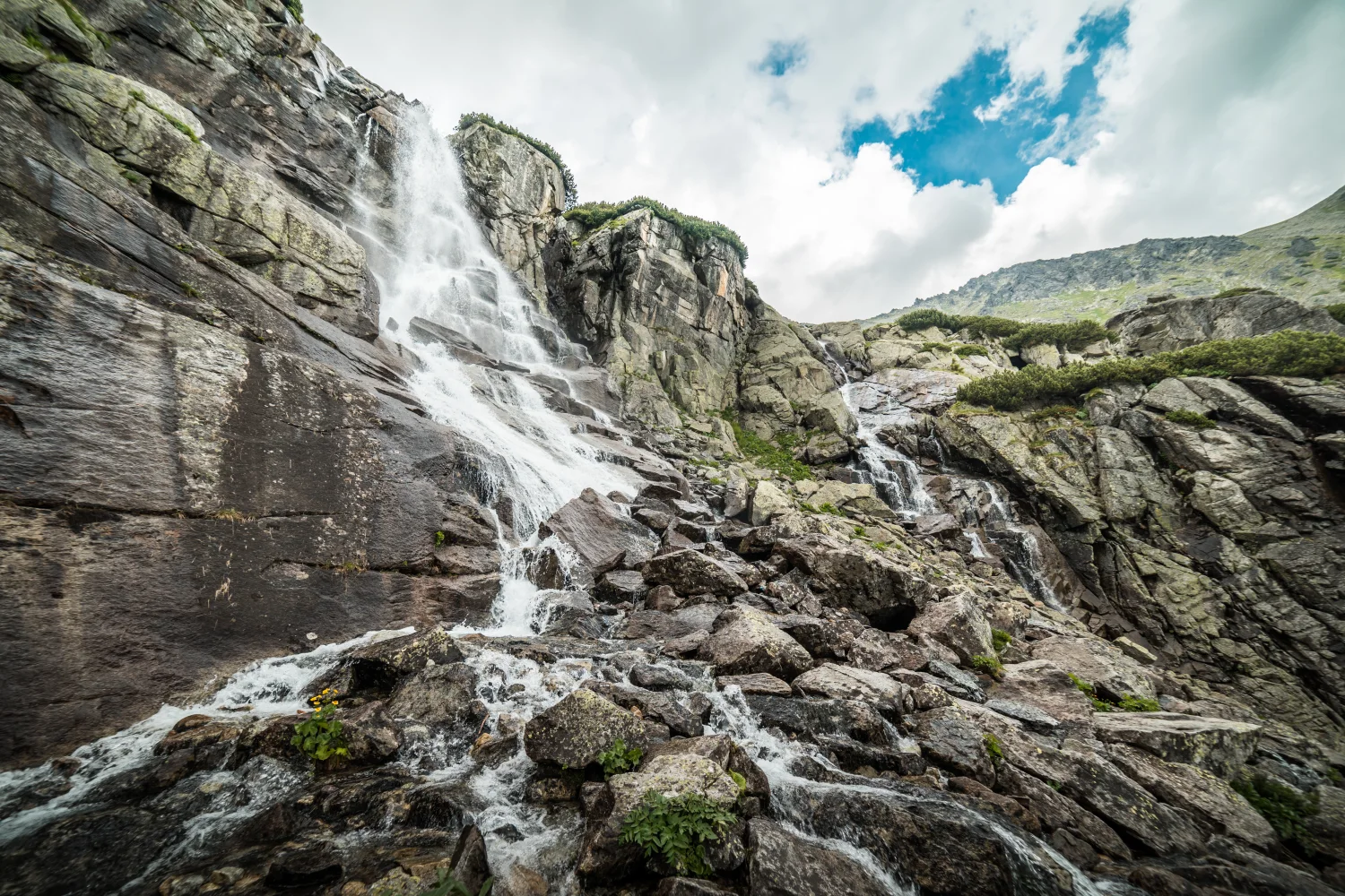 Wasserfall fließt über Steine vor dem Himmel mit weißen Wolken