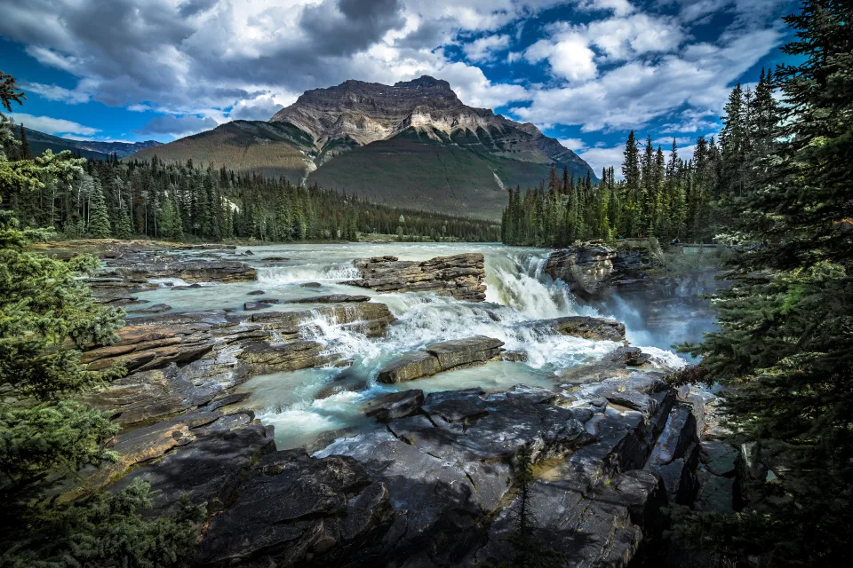 Wasserfall fließt über Steine vor einer Bergkulisse, Kanada