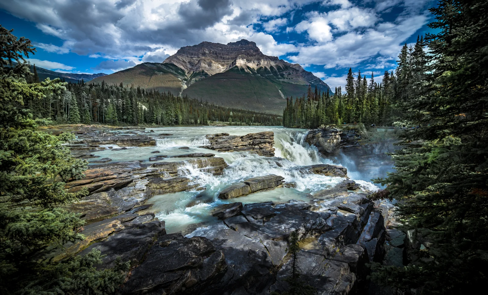 Wasserfall fließt über Steine vor einer Bergkulisse, Kanada