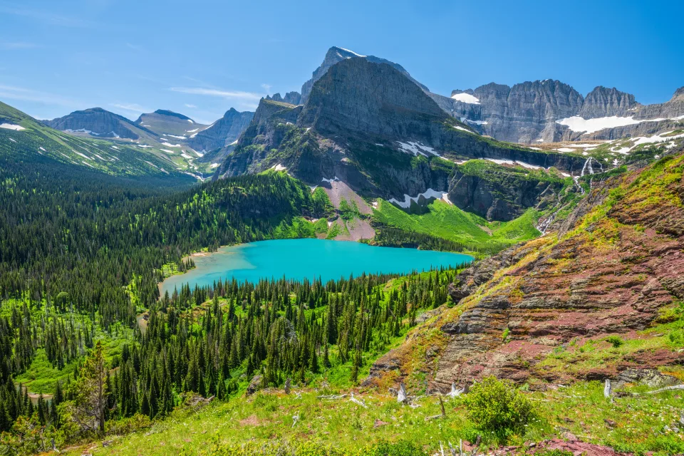 Blick von oben auf hellblaues See und Berge unter hellblauem Himmel