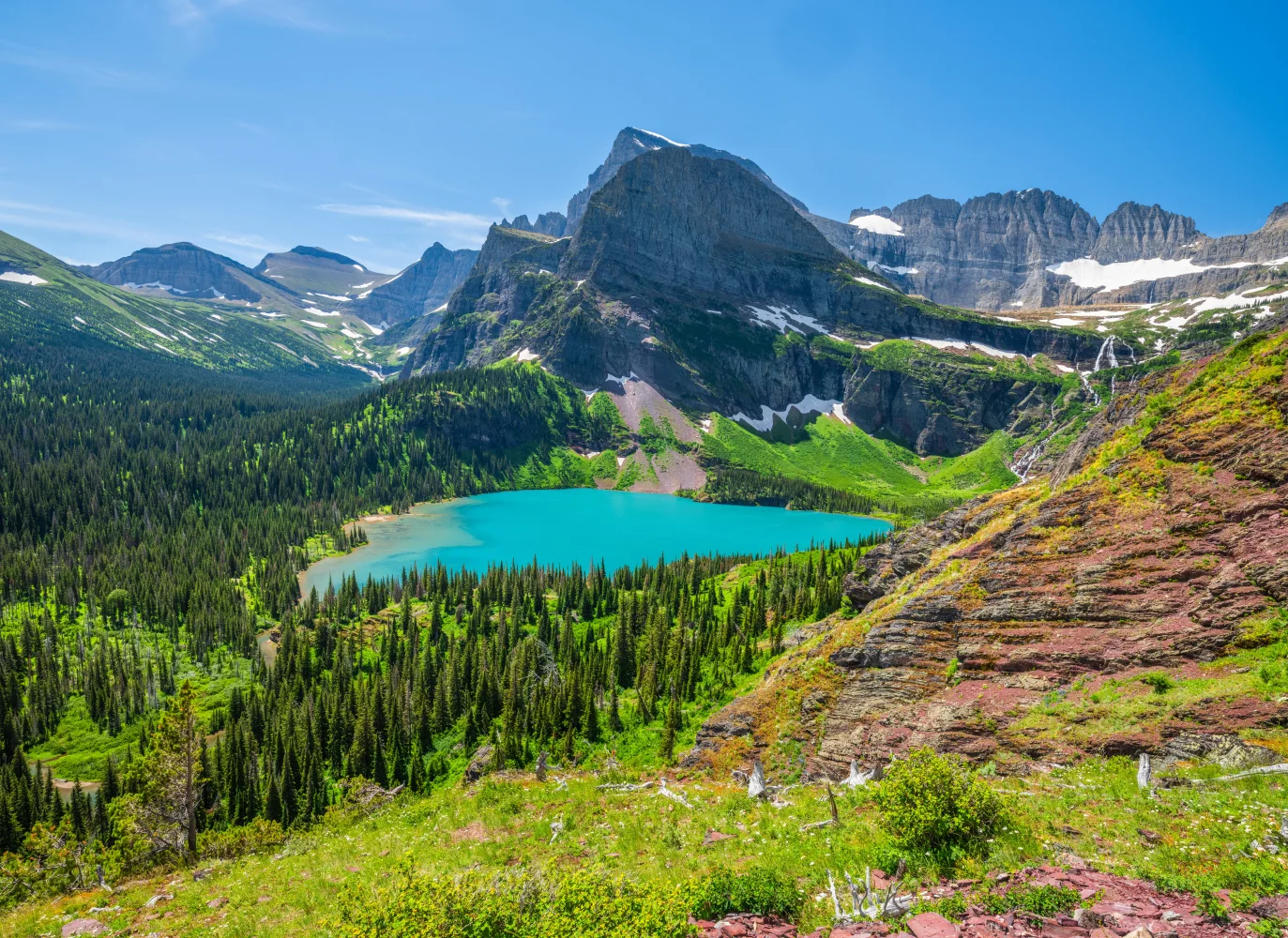 Blick von oben auf hellblaues See und Berge unter hellblauem Himmel