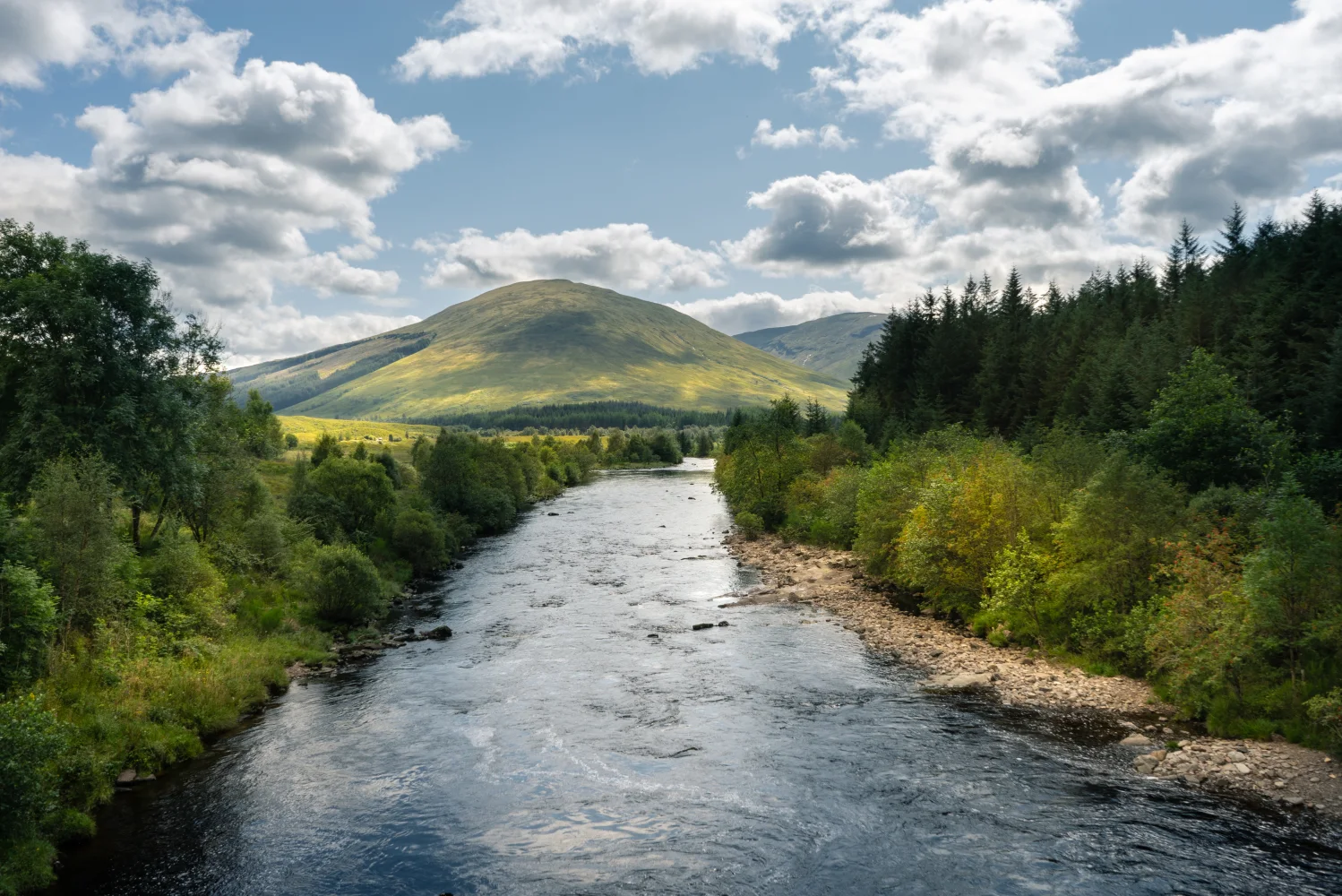 Weiße Wolken in hellblauem Himmel über Fluss in den Bergenn