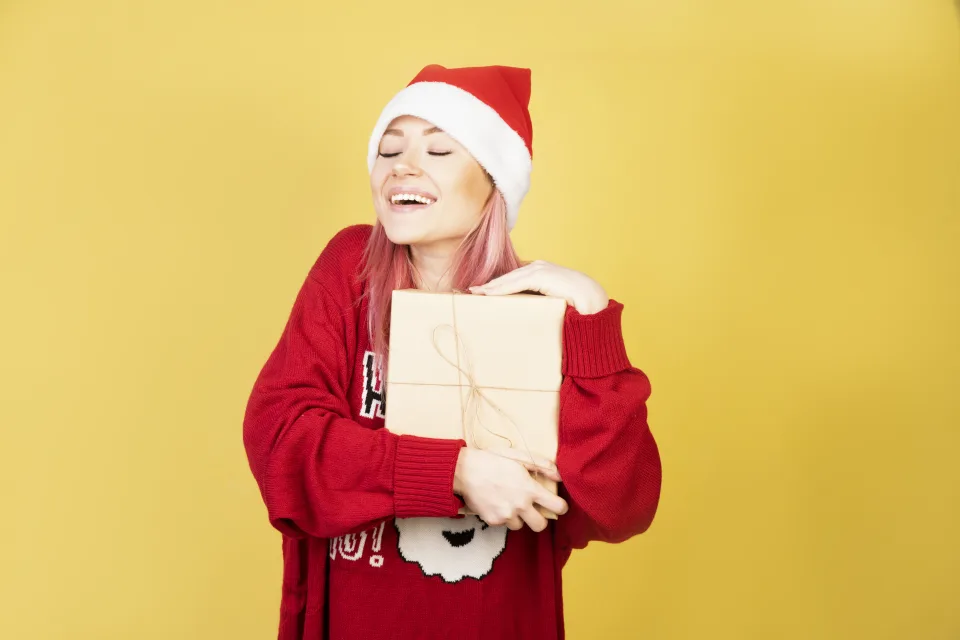 Lächelnde Frau in rotem Pullover mit einem Geschenk vor gelbem Hintergrund