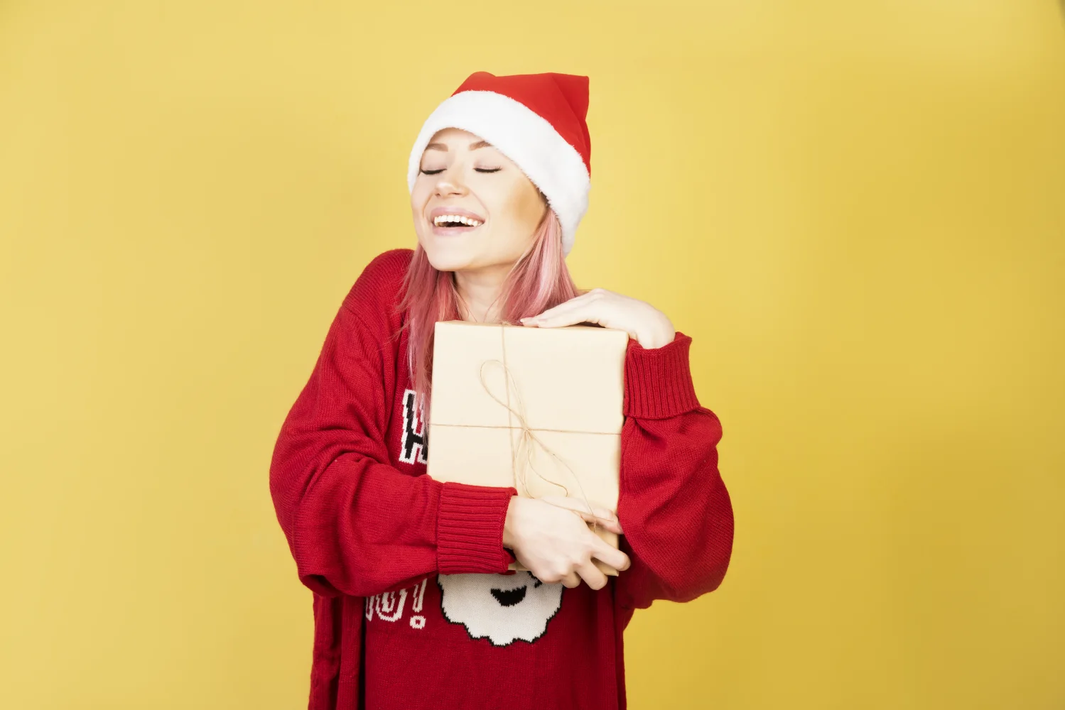 Lächelnde Frau in rotem Pullover mit einem Geschenk vor gelbem Hintergrund