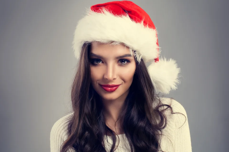 Schöne Brünette mit Weihnachtsmütze vor grauem Hintergrund