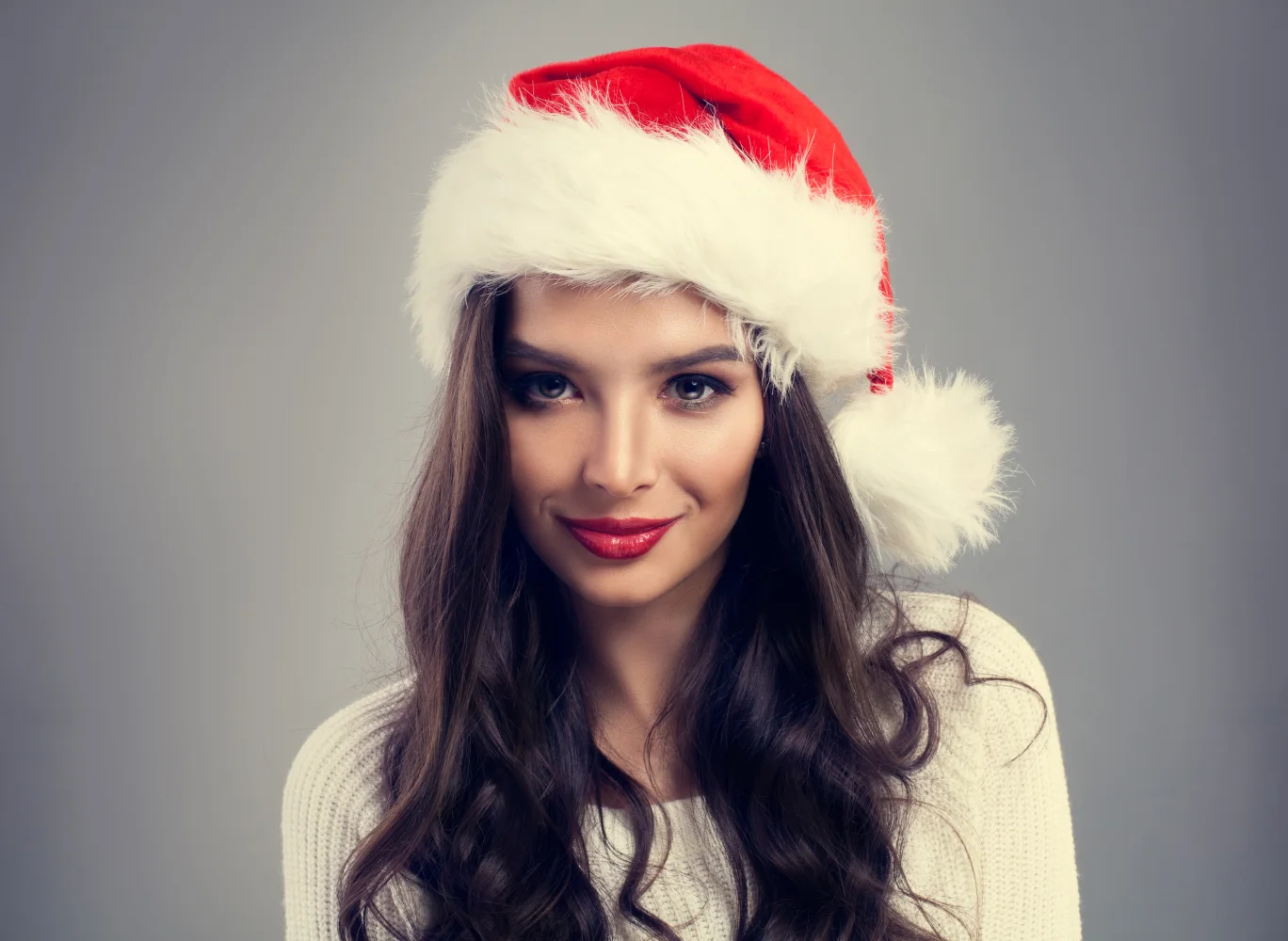 Schöne Brünette mit Weihnachtsmütze vor grauem Hintergrund