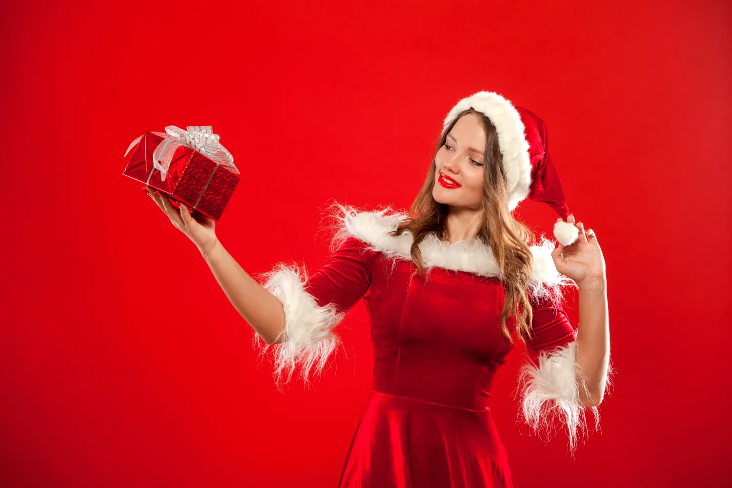 Schöne Schneemädchen mit einem Geschenk in Hand vor rotem Hintergrund