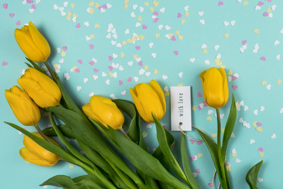 Blumenstrauß gelben Tulpen mit kleinen Herzen vor hellblauem Hintergrund