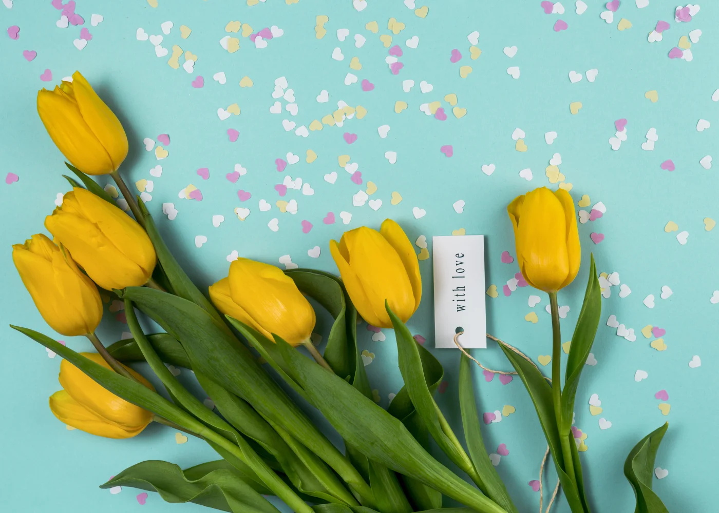 Blumenstrauß gelben Tulpen mit kleinen Herzen vor hellblauem Hintergrund