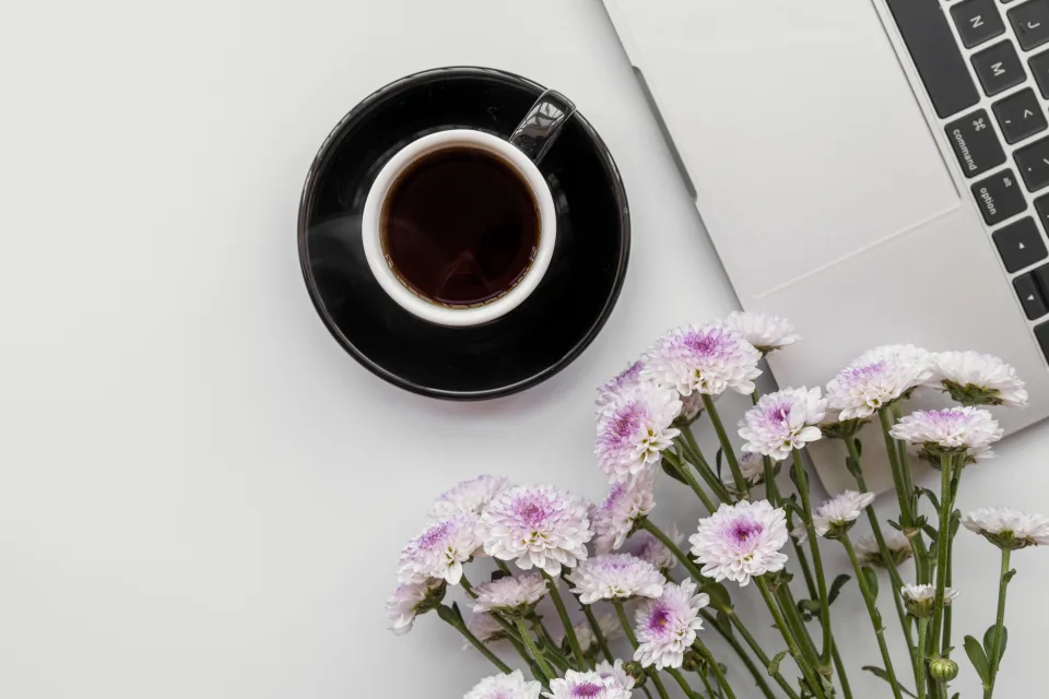 Rosa Chrysanthemen mit Tasse Kaffee und Laptop auf Tisch