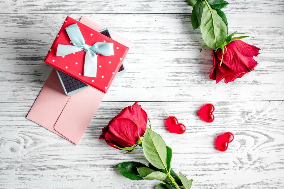 Zwei rote Rose mit einem Geschenk und Herzen auf Tisch